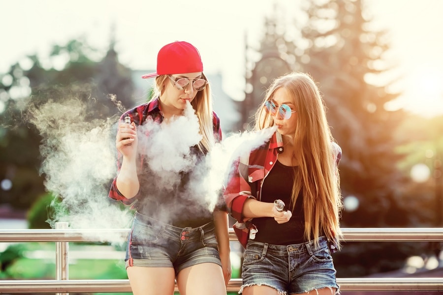Two women vaping outdoor. The evening sunset over the city. Toned image