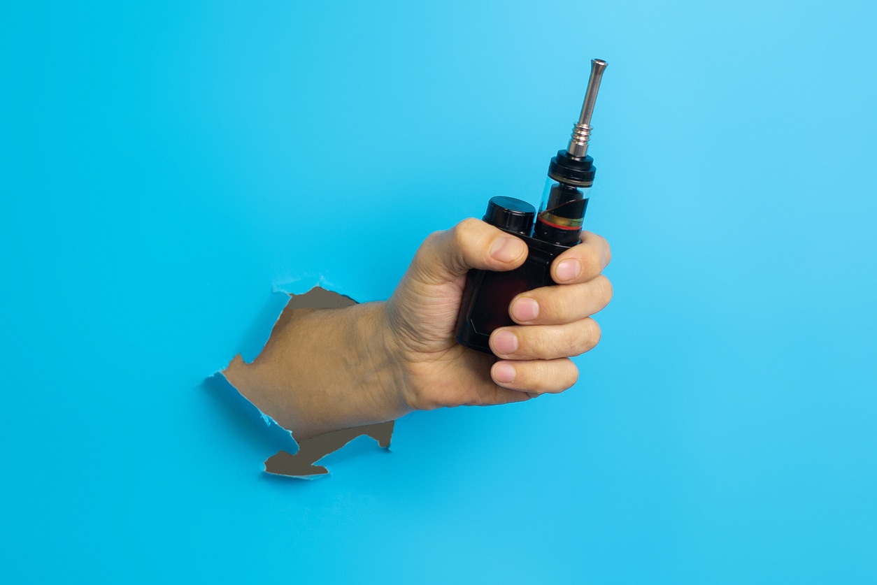 Vape device in man's hand on blue background. Vaping concept