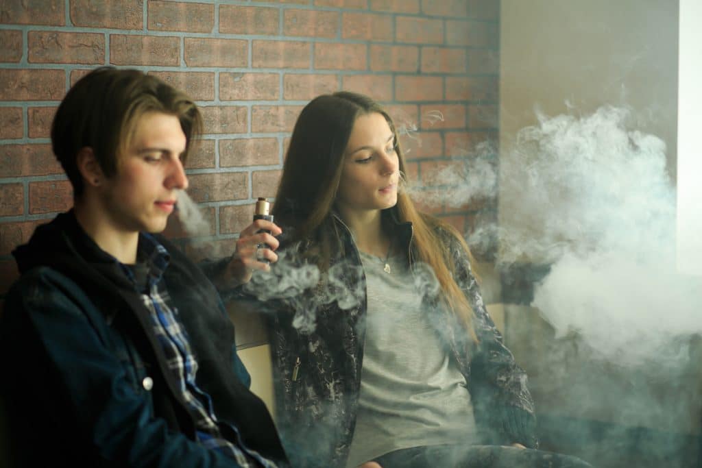 Vape teenagers. Young cute girl in sunglasses and young handsome guy smoke an electronic cigarettes in the vape bar. Bad habit that is harmful to health.