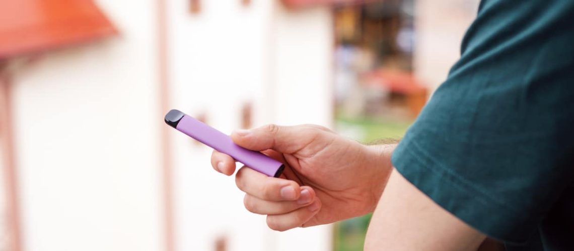Disposable electronic cigarettes of different flavors in hand on a Light Violet background. The concept of modern smoking, vaping and nicotine.
