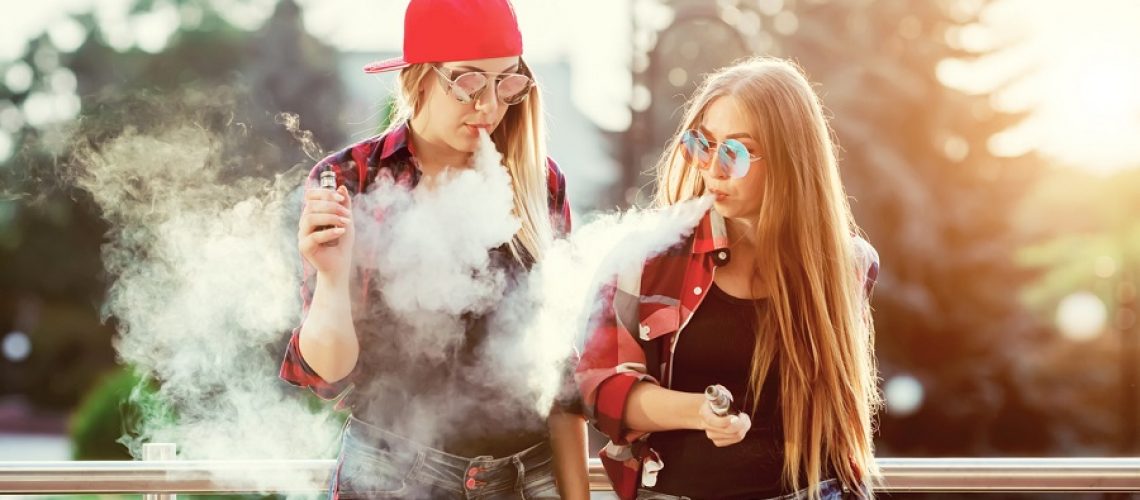Two women vaping outdoor. The evening sunset over the city. Toned image